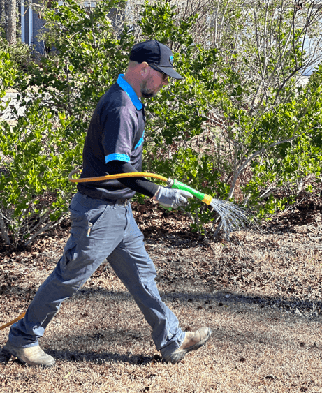 Neon technician applying a lawn treatment along a shrub bed