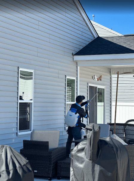 A Neon Pest and Lawn employee sprays a house with a hose, providing pest control services in Aynor.