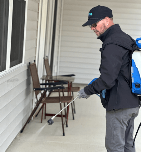 A Neon Pest and Lawn employee sprays pesticide on a house