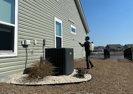 A Neon Pest and Lawn employee stands in the backyard. And he is providing commercial pest control service for his client's commercial building.