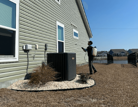 A man from Neon Pest and Lawn holds a hose outside a house
