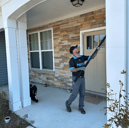 A man from Neon Pest and Lawn is cleaning a house's exterior, highlighting their pest control service in Myrtle Beach.