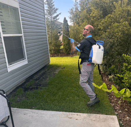 A man in a backpack sprays lawn treatment for scorpion control