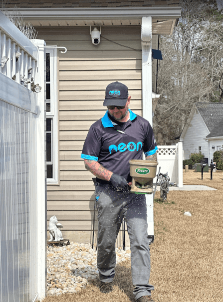 A man in a blue shirt and black hat holds a bag, representing Neon Pest and Lawn's pest control services in Longs.