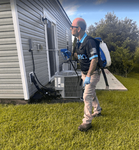 An employee in blue attire sprays a house, providing scorpion control service for Neon Pest and Lawn.