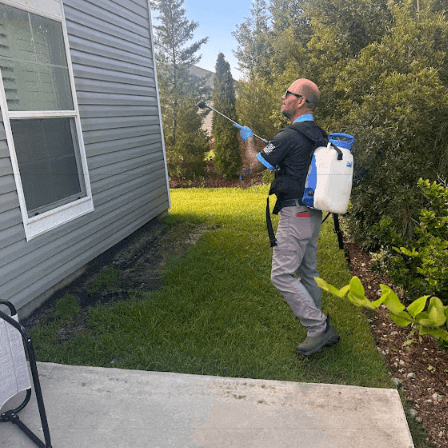 An employee of Neon Pest and Lawn uses a garden hose to spray a lawn
