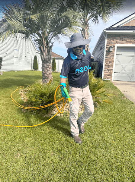 An employee of Neon Pest and Lawn waters a palm tree with a hose, showcasing their lawn care service in North Myrtle Beach.