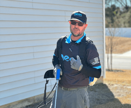An employee of Neon Pest and Lawn, wearing a black shirt and blue hat, holds a bag for rodent control at a client's residence.