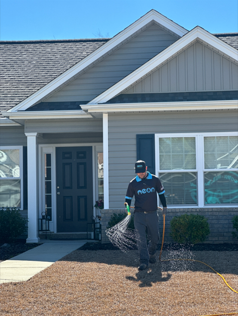 An employee of Neon Pest and Lawn waters a lush residential lawn outside a well-maintained house.