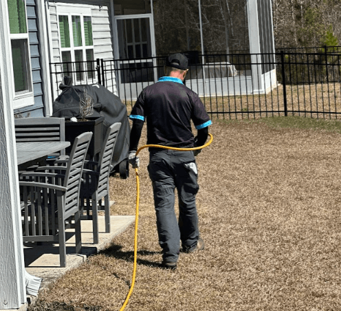 A man cleans the yard with a hose, preparing for lawn fertilizer service to enhance the grass's health and appearance.