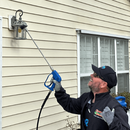 A Neon Pest and Lawn employee power washing a house's exterior to eliminate pests and enhance cleanliness.