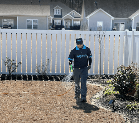 A Neon Pest and Lawn employee watering a lush residential lawn in a well-maintained backyard.