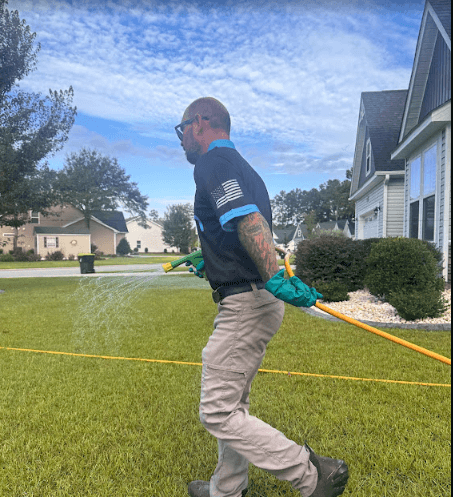A Neon Pest and Lawn employee in a blue shirt sprays grass, showcasing residential lawn care services.