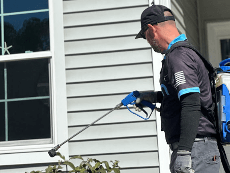 A Neon Pest and Lawn employee sprays mosquito control treatment on a client's house while wearing a backpack.