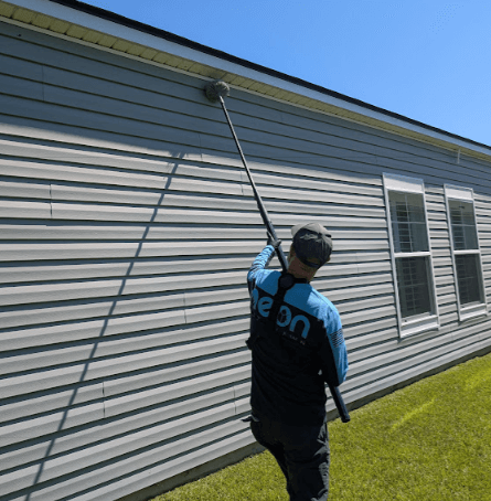Neon Pest and Lawn employee uses a hose to apply ant control treatment on a client's house siding.